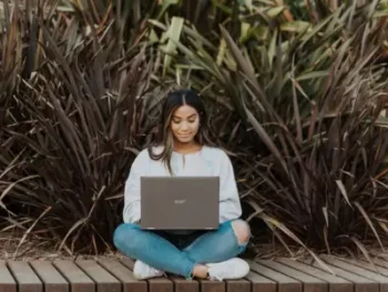 Woman sitting with computer in a meditative pose - Friday online meditation class